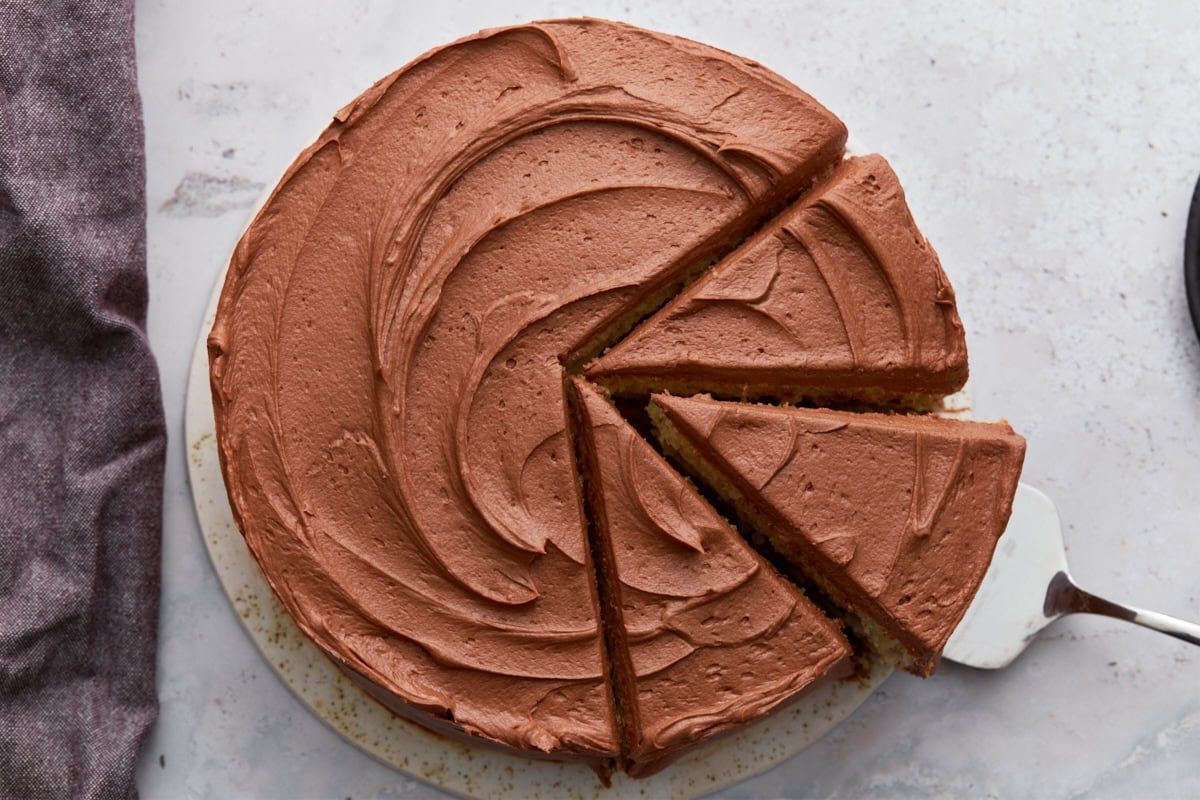 Overhead view of a chocolate-frosted yellow cake with several slices cut, revealing the two-layer interior.