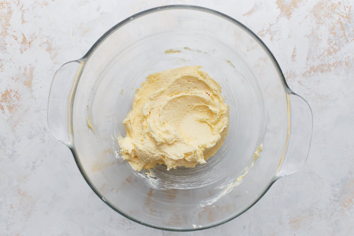 Smooth pale yellow cake batter in a glass mixing bowl after adding eggs and mixing.