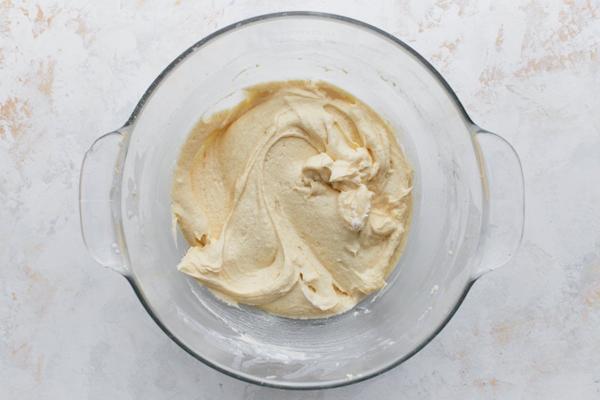 Thick, creamy yellow cake batter in a glass mixing bowl, ready to be poured into pans.