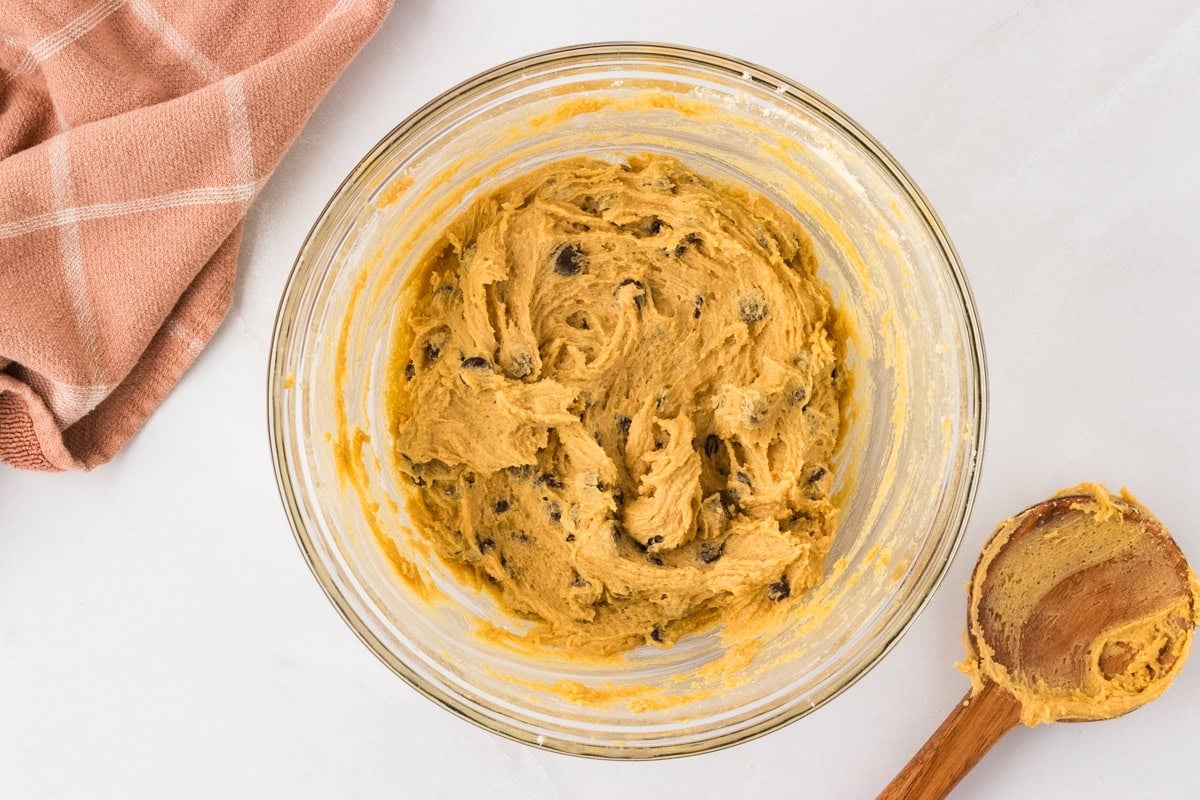 Cookie dough mixed with chocolate chips in a glass bowl with a wooden spoon.