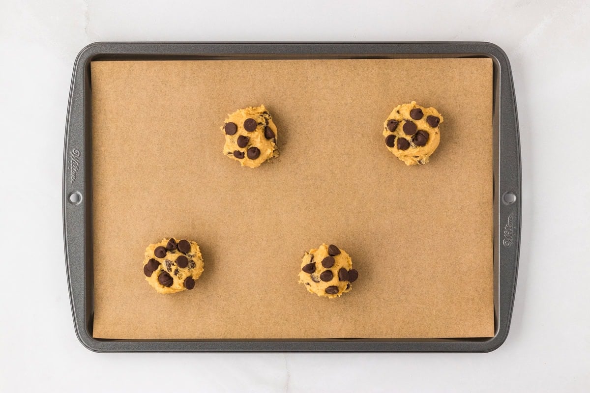 Four scoops of chickpea chocolate chip cookie dough placed on a parchment-lined baking sheet.