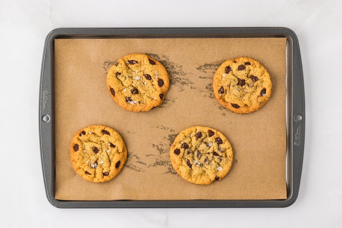 Four freshly baked chickpea chocolate chip cookies on a parchment-lined baking sheet.