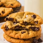 Stack of chickpea chocolate chip cookies on a plate with one broken in half, showing melted chocolate chips inside.