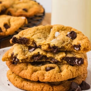 Stack of chickpea chocolate chip cookies on a plate with one broken in half, showing melted chocolate chips inside.