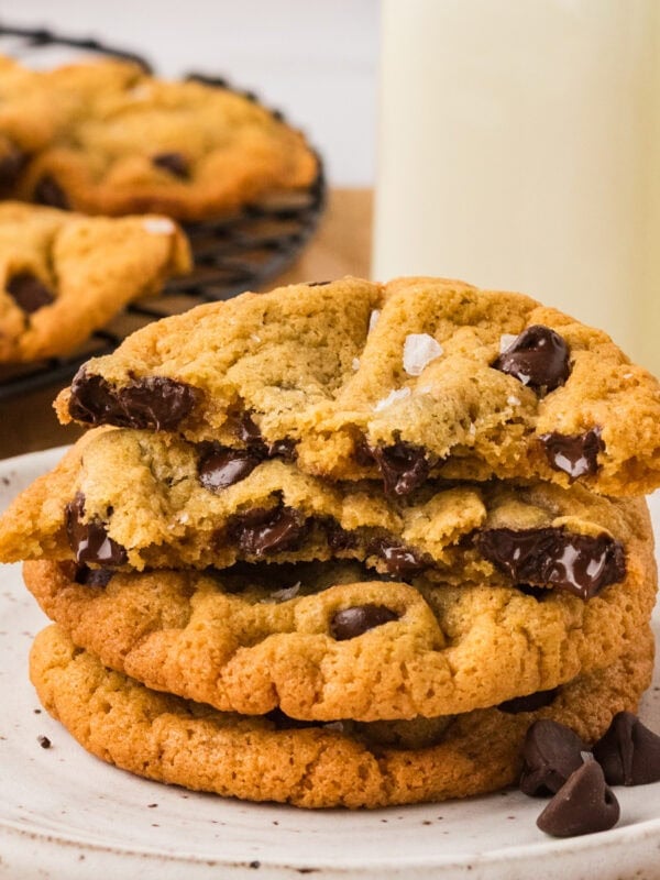 Stack of chickpea chocolate chip cookies on a plate with one broken in half, showing melted chocolate chips inside.