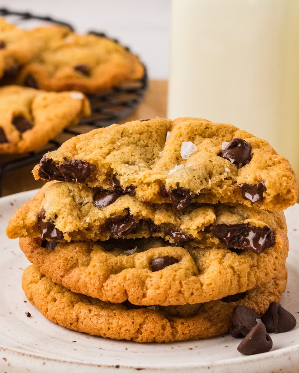 Stack of chickpea chocolate chip cookies on a plate with one broken in half, showing melted chocolate chips inside.
