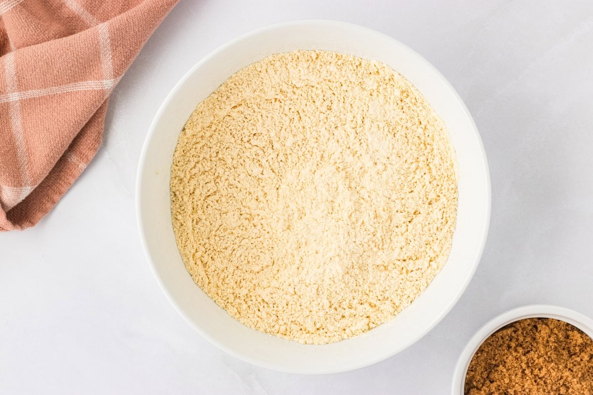 Bowl of chickpea flour on a white countertop with a brown napkin beside it.