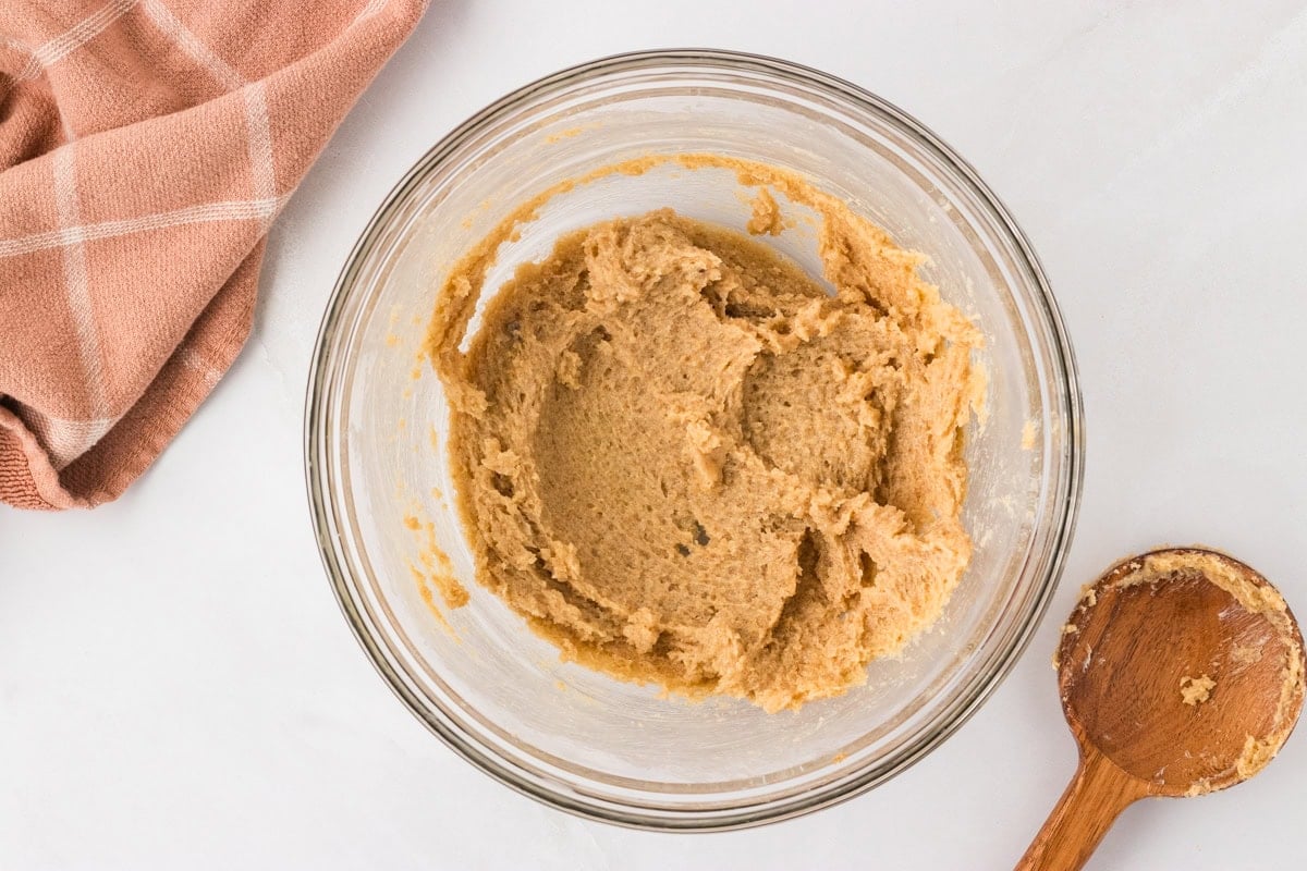 Creamed butter and sugar mixture in a glass mixing bowl with a wooden spoon.