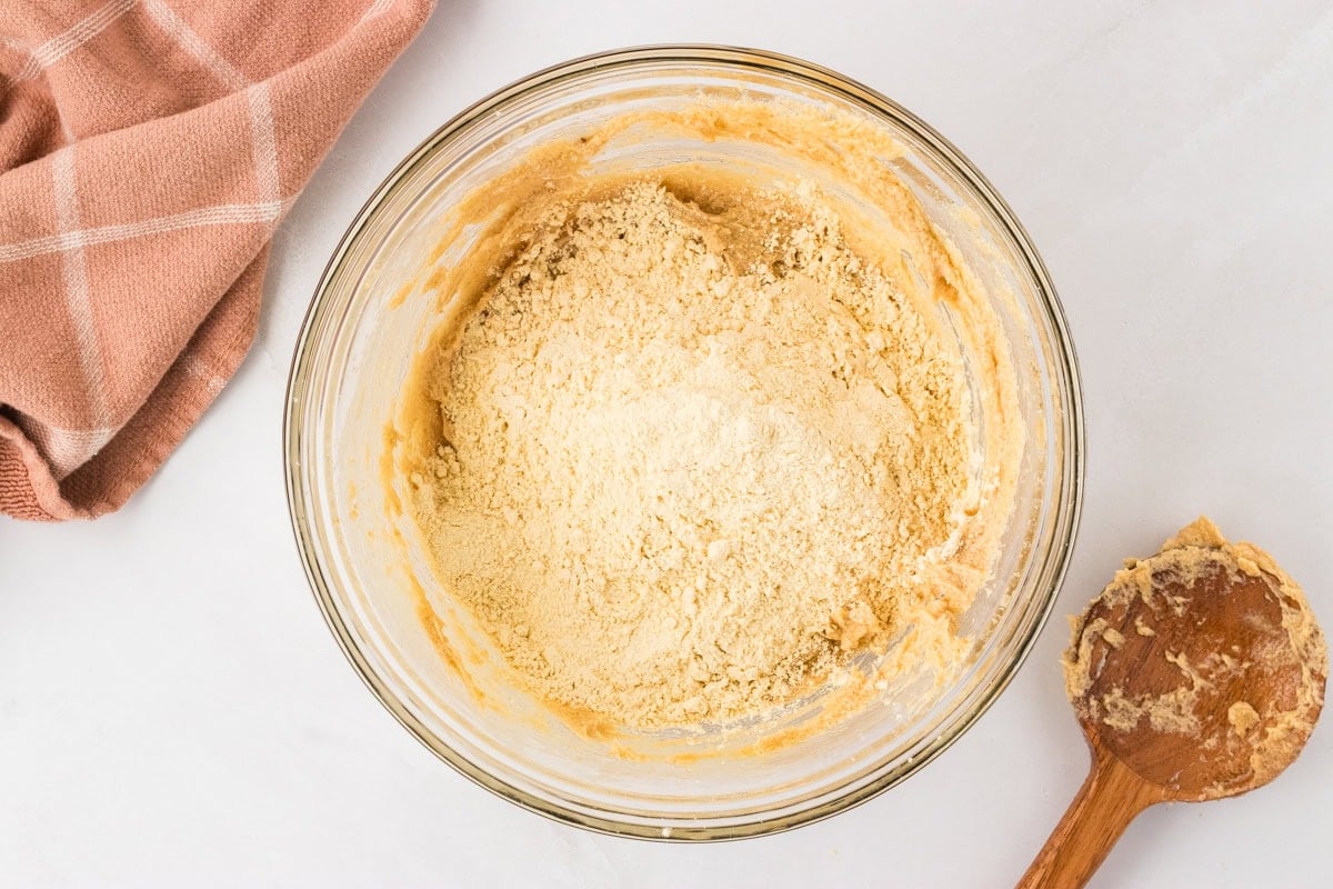 Chickpea flour being added to the wet mixture in a glass mixing bowl.