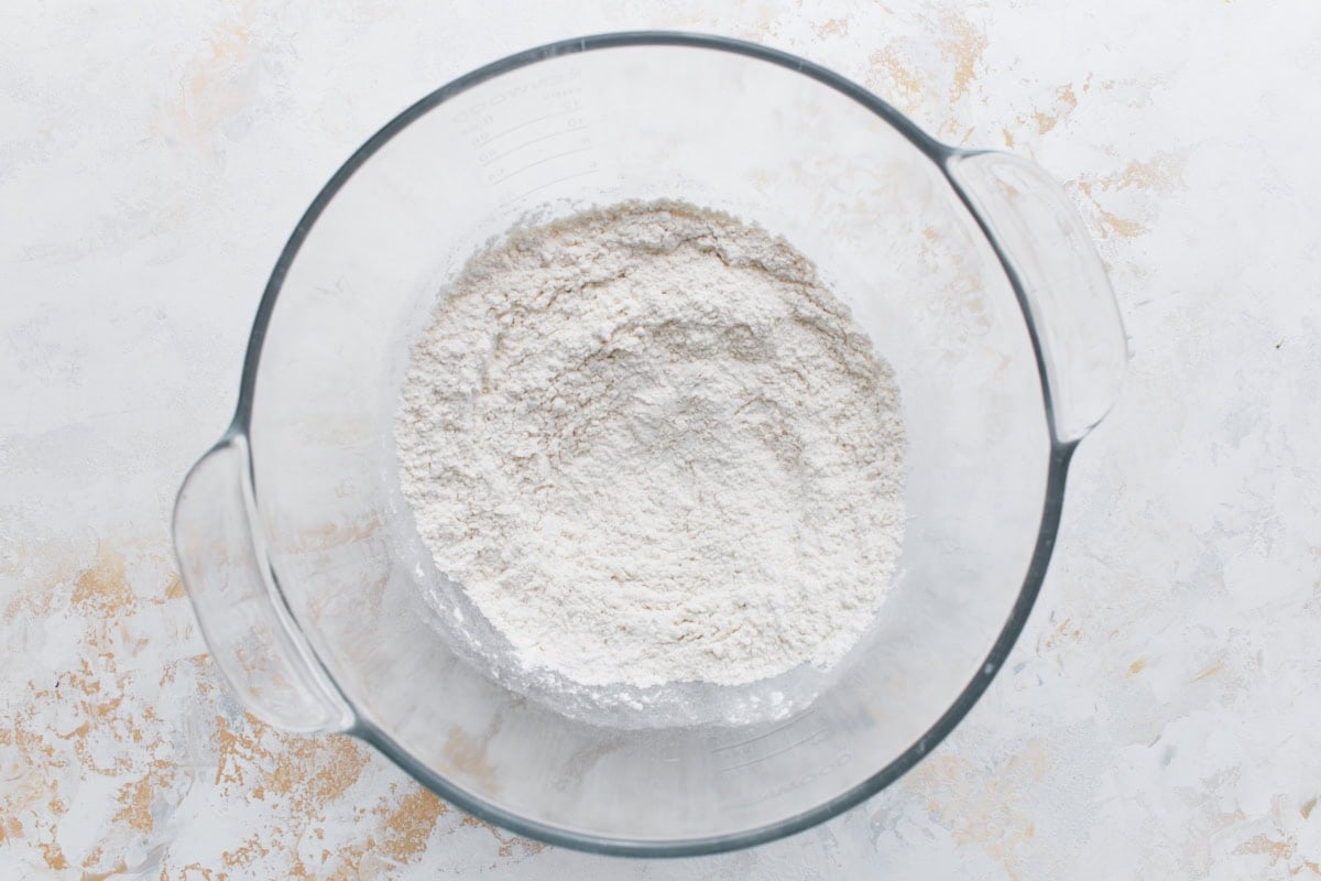 A glass mixing bowl filled with gluten-free flour, yeast, sugar, and salt before adding wet ingredients.