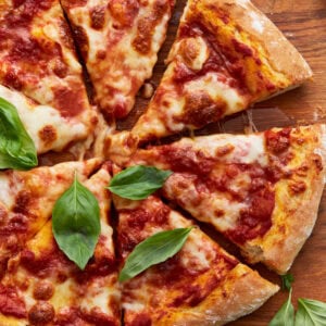 A baked vegan pizza sliced into wedges, topped with tomato sauce, melted vegan cheese, and fresh basil leaves on a wooden board.