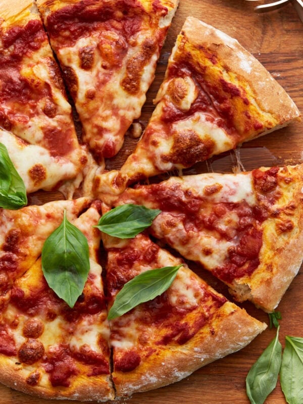 A baked vegan pizza sliced into wedges, topped with tomato sauce, melted vegan cheese, and fresh basil leaves on a wooden board.