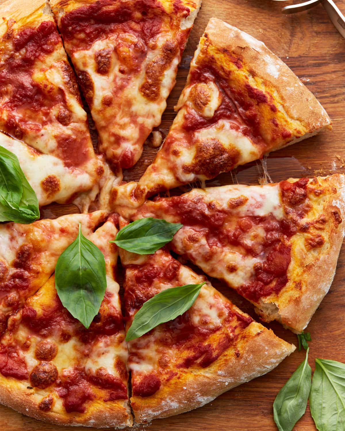 A baked vegan pizza sliced into wedges, topped with tomato sauce, melted vegan cheese, and fresh basil leaves on a wooden board.
