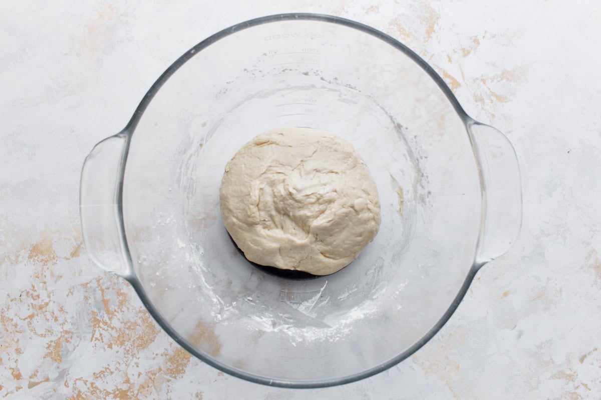 A smooth ball of pizza dough resting in a glass bowl after kneading.