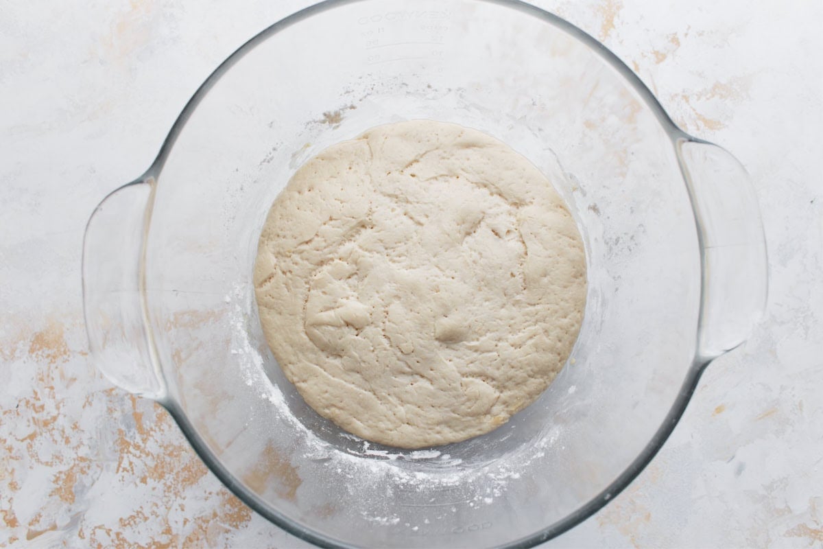 The risen gluten-free dough in a glass bowl, doubled in size and airy with small bubbles on the surface.