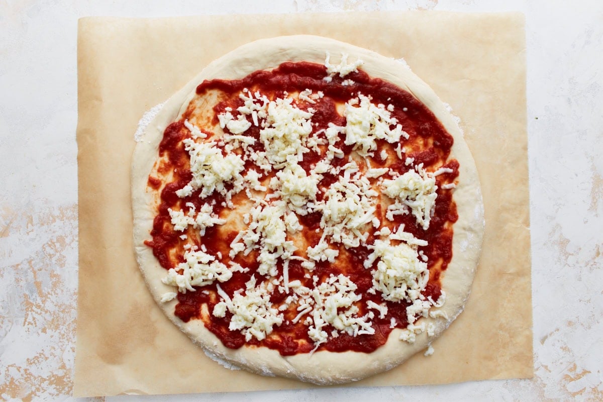 The pizza dough topped with tomato sauce and scattered shredded vegan cheese before baking.