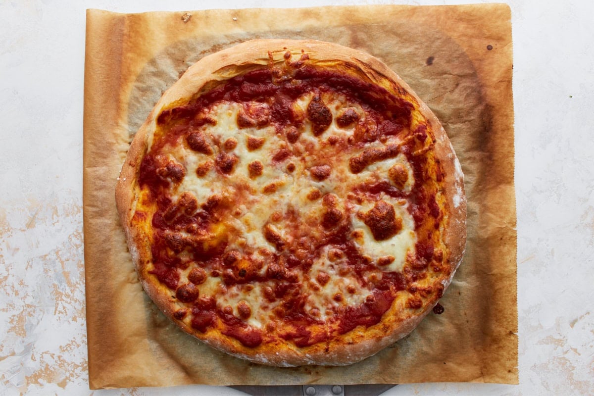 A golden-brown vegan pizza fresh out of the oven on parchment paper, cheese melted across the surface.