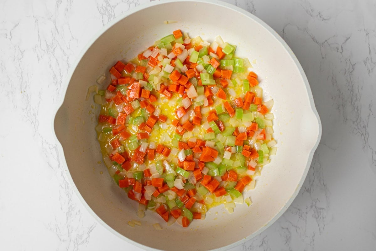 Diced onions, carrots, and celery sautéing in butter and olive oil in a skillet.
