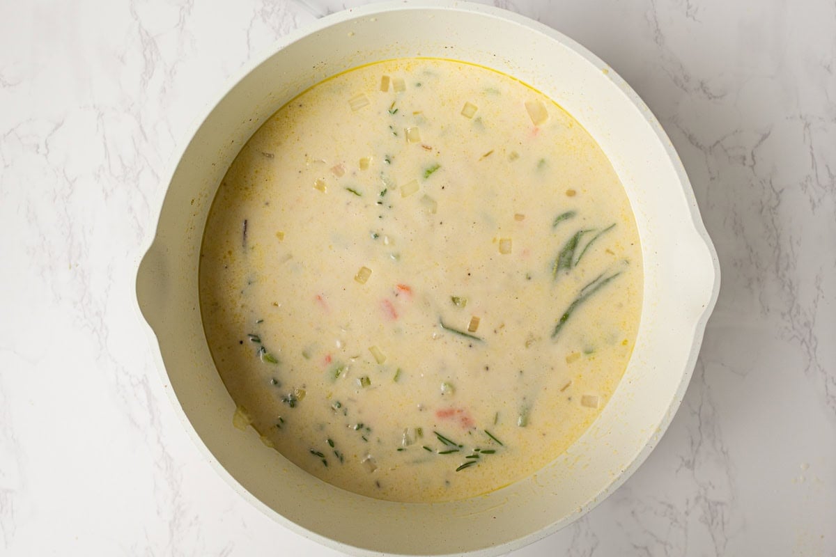 Creamy broth mixture simmering with fresh rosemary, thyme, and sage sprigs.