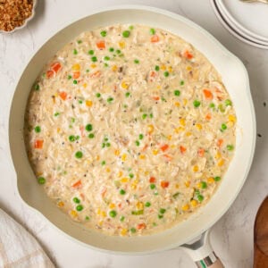 Creamy crustless chicken pot pie filling simmering in a skillet with peas, carrots, corn, and chicken.