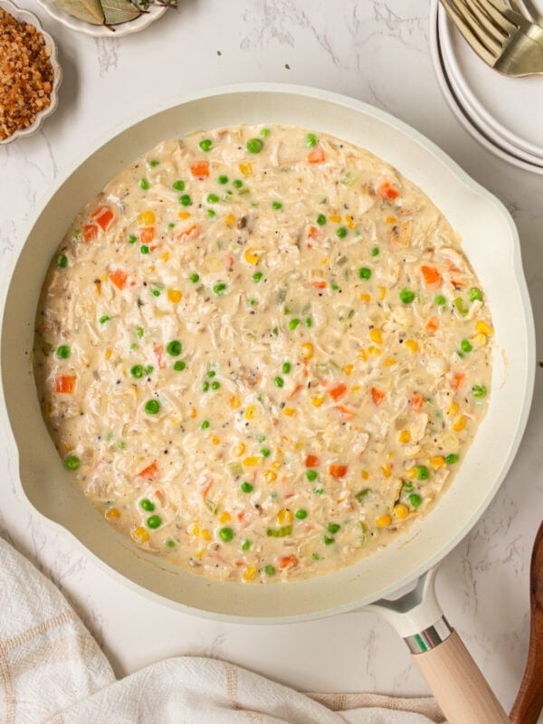 Creamy crustless chicken pot pie filling simmering in a skillet with peas, carrots, corn, and chicken.