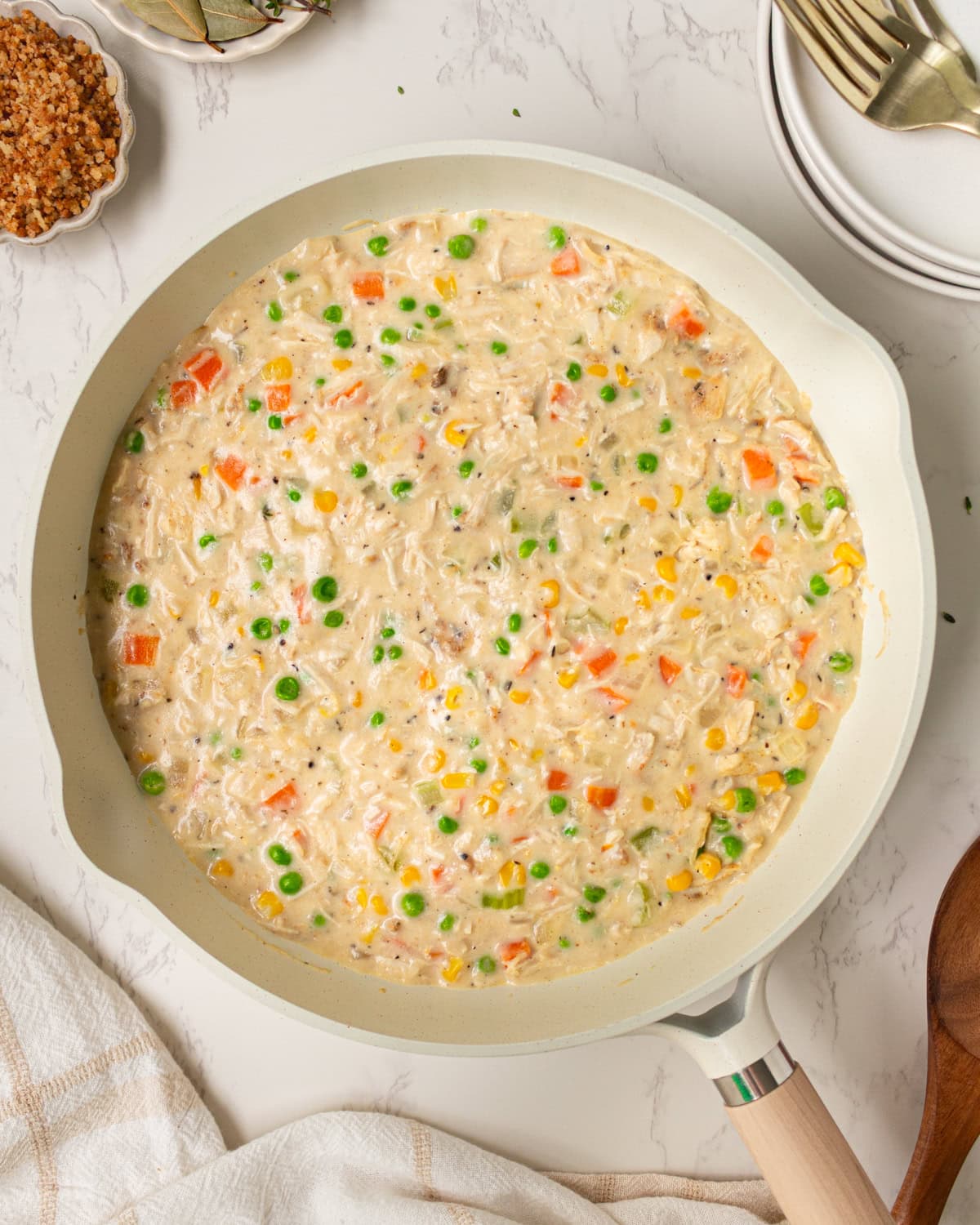 Creamy crustless chicken pot pie filling simmering in a skillet with peas, carrots, corn, and chicken.