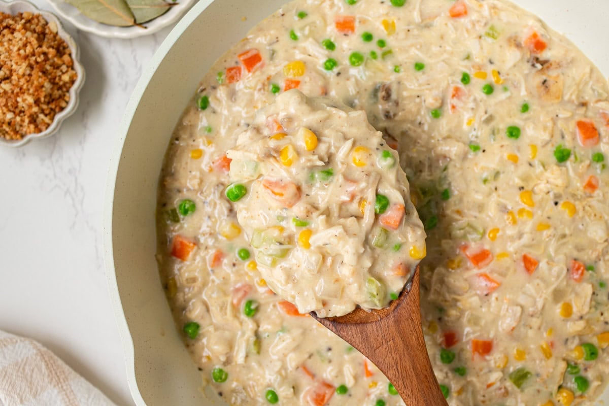Wooden spoon lifting a hearty serving of creamy crustless chicken pot pie filling.