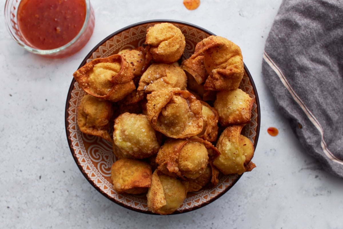 gluten free crab rangoons served in a bowl with chili sauce nearby