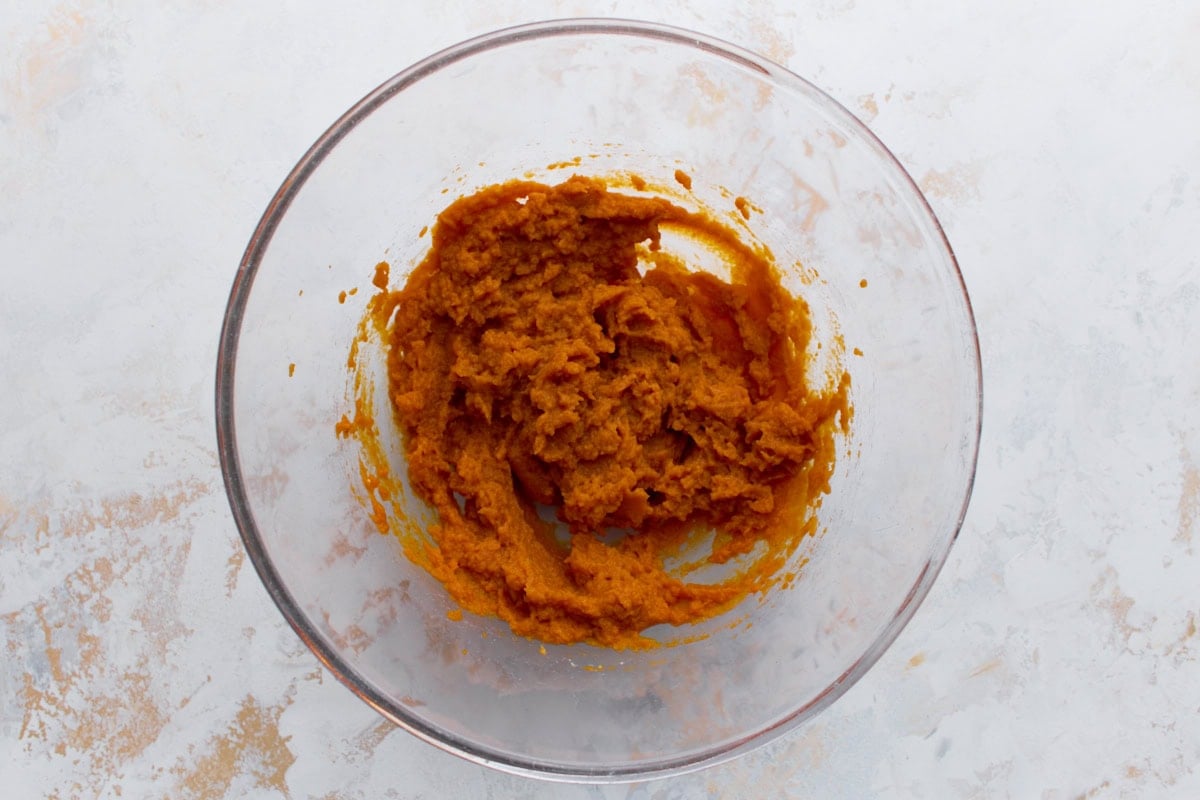 Glass mixing bowl with canned pumpkin puree partially mixed, sitting on a light counter.