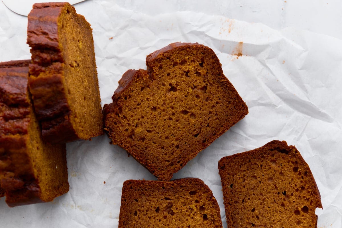 Close-up slices of gluten-free pumpkin bread laid out on parchment, highlighting the moist texture.