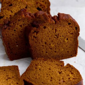 Slices of moist gluten-free pumpkin bread on parchment paper, showing a soft crumb and golden-brown crust.