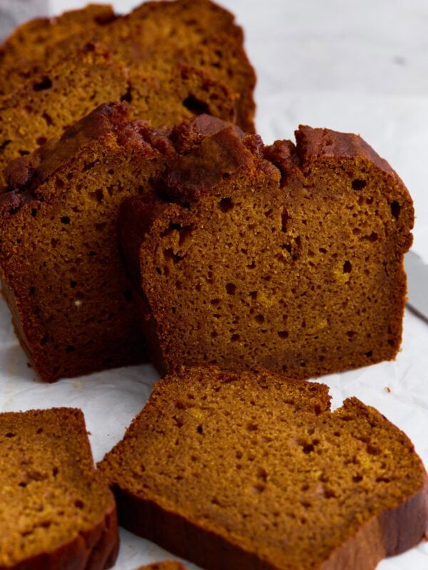 Slices of moist gluten-free pumpkin bread on parchment paper, showing a soft crumb and golden-brown crust.
