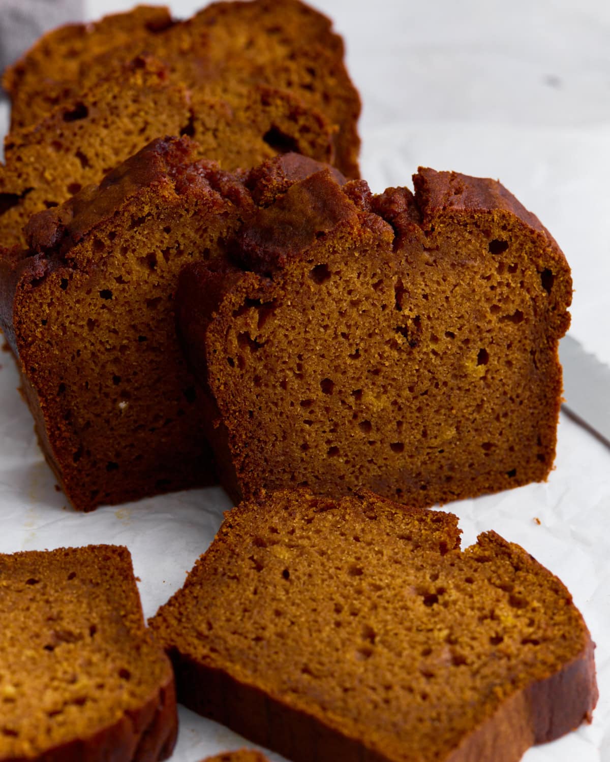 Slices of moist gluten-free pumpkin bread on parchment paper, showing a soft crumb and golden-brown crust.