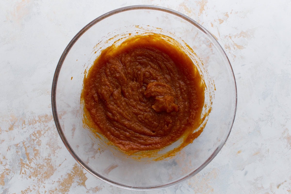 Pumpkin puree mixed with sugars and vanilla in a glass bowl, creating a smooth orange base.