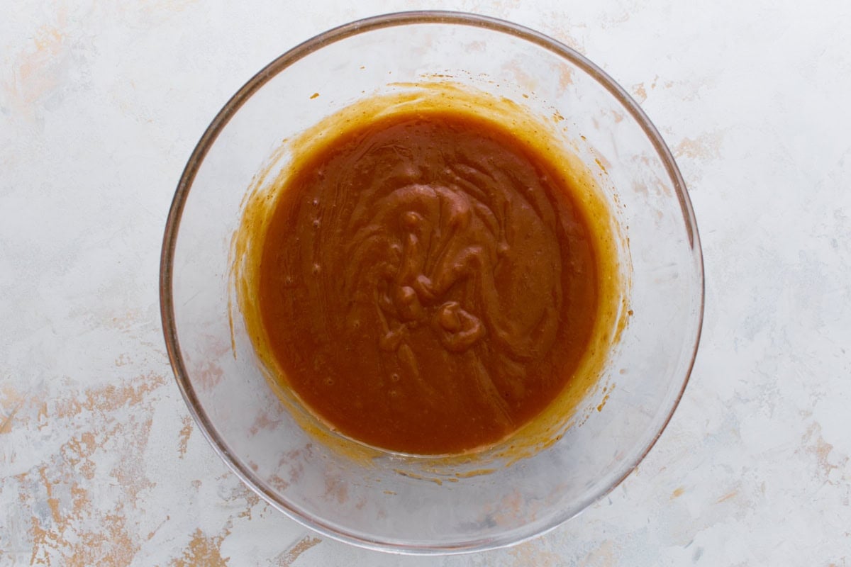 Pumpkin mixture whisked with eggs and oil in a clear bowl until glossy and smooth.