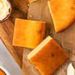 Overhead view of keto cornbread squares on parchment paper, golden brown with a small dish of butter and a butter knife nearby.