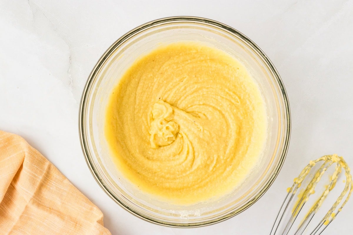 Smooth yellow cornbread batter in a glass bowl after mixing, with a whisk resting nearby.