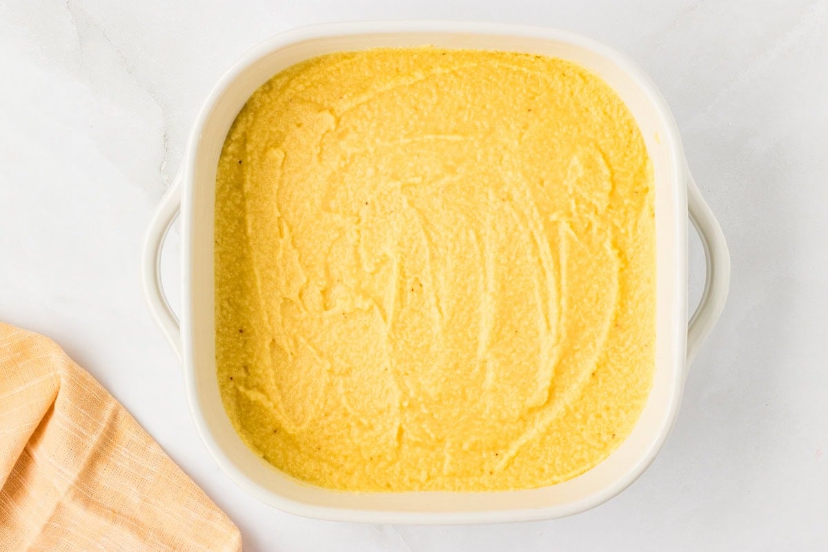 Cornbread batter spread evenly in a white baking dish before going into the oven.