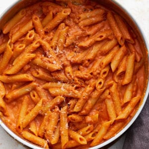 A pan filled with gluten-free penne pasta coated in creamy vegan vodka sauce, sprinkled lightly with vegan parmesan.