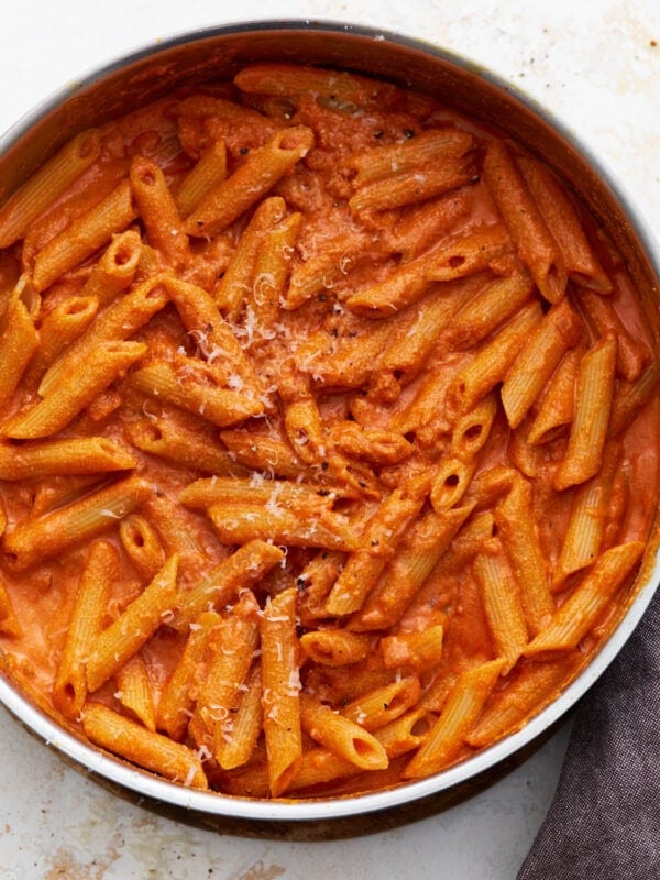 A pan filled with gluten-free penne pasta coated in creamy vegan vodka sauce, sprinkled lightly with vegan parmesan.