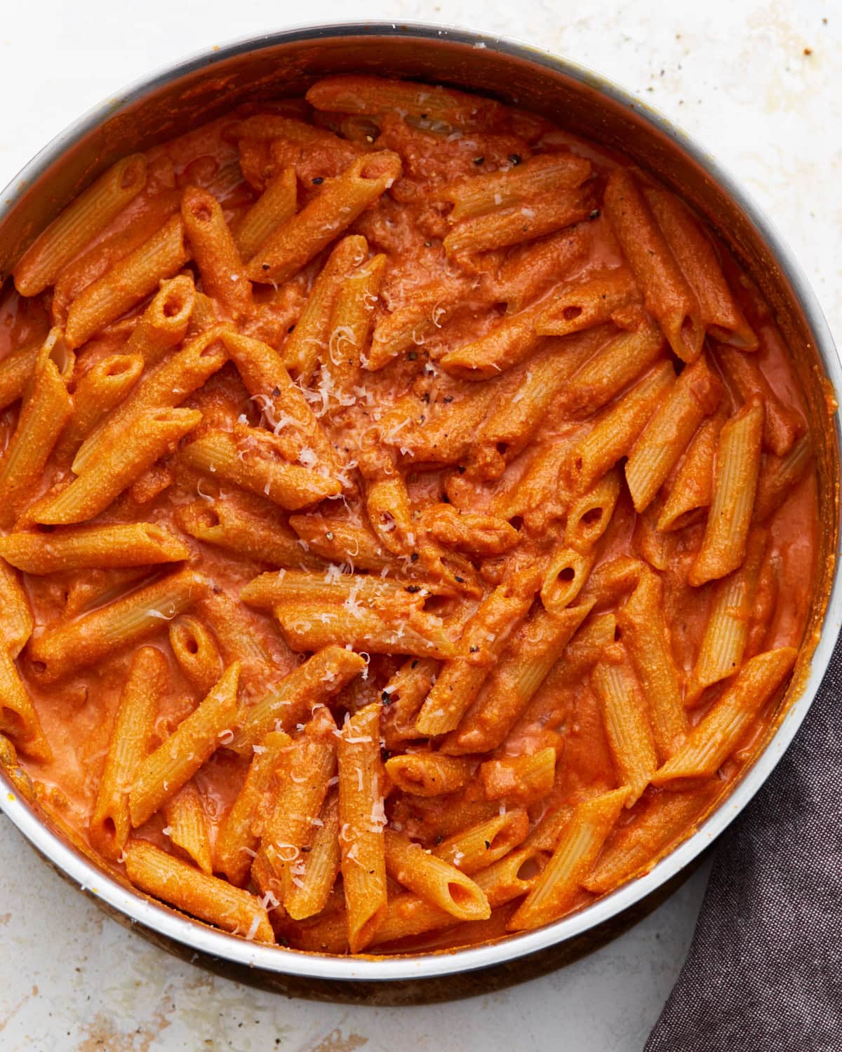 A pan filled with gluten-free penne pasta coated in creamy vegan vodka sauce, sprinkled lightly with vegan parmesan.