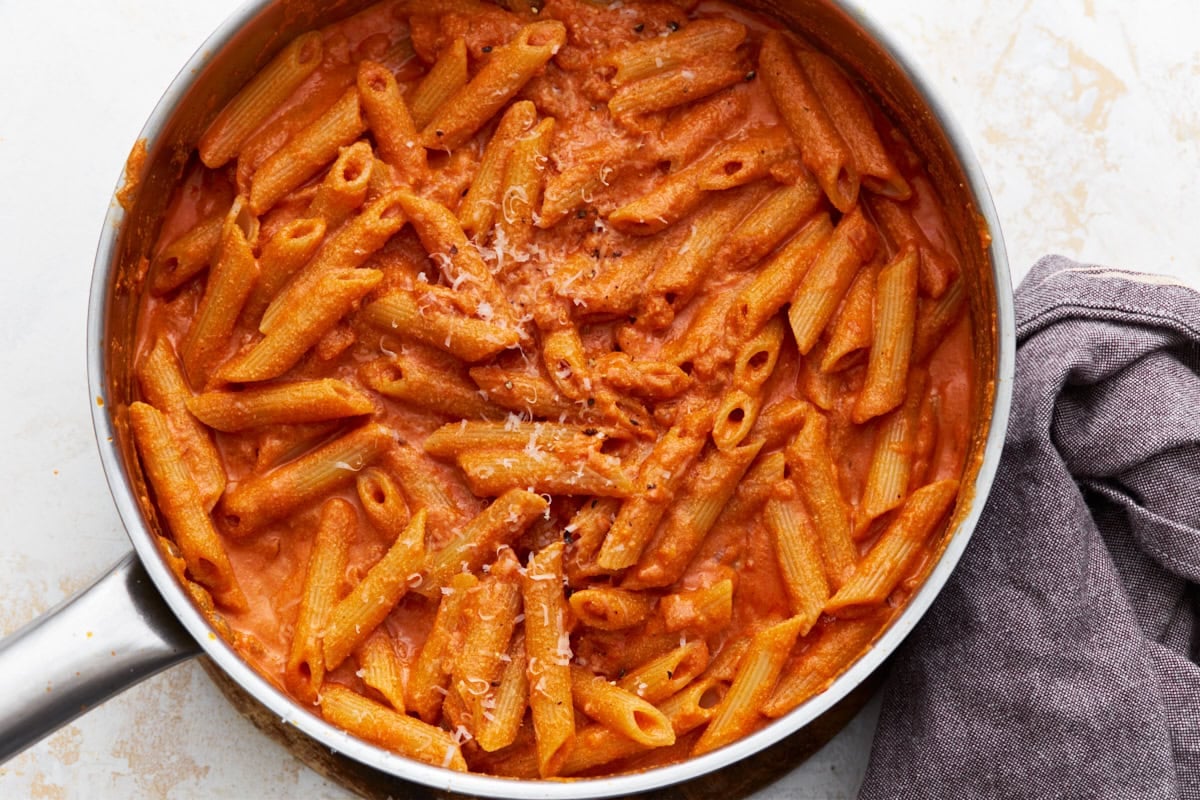 Finished vegan vodka pasta in a skillet, garnished with vegan parmesan, with a cloth napkin on the side.