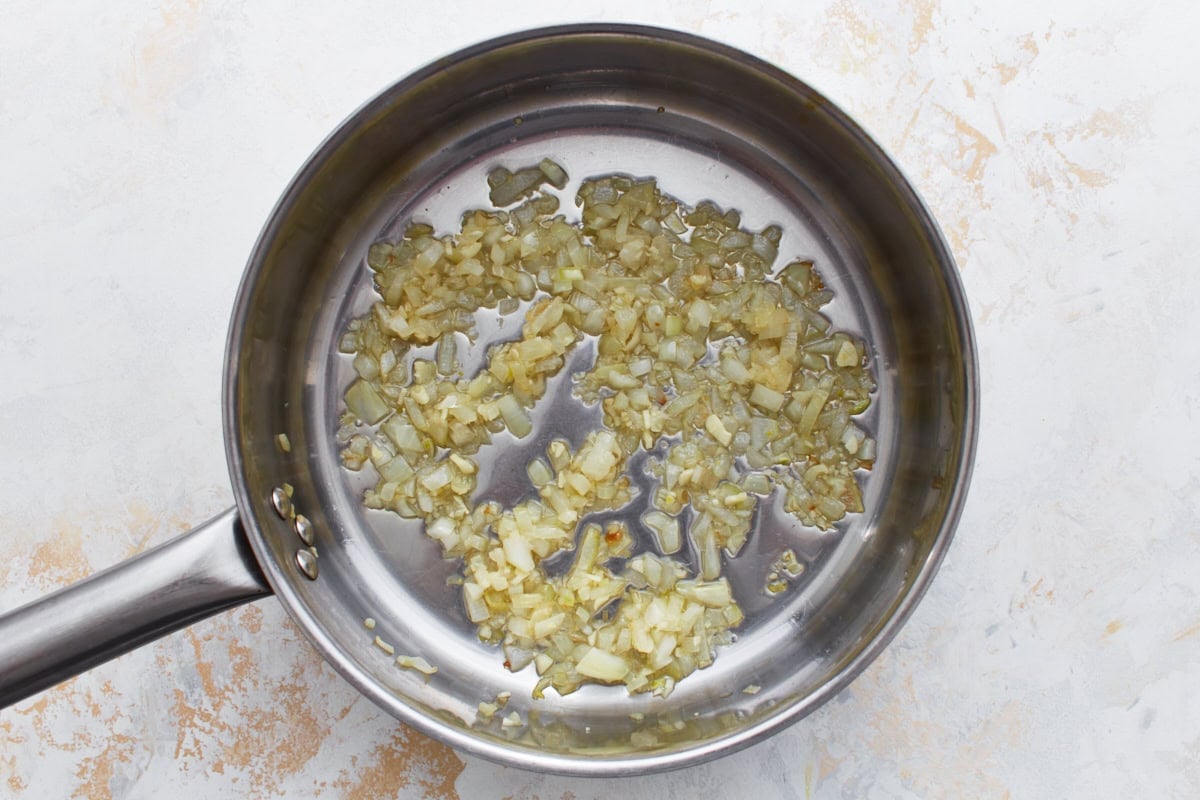 Chopped onions and garlic sautéing in olive oil in a stainless steel skillet until softened.