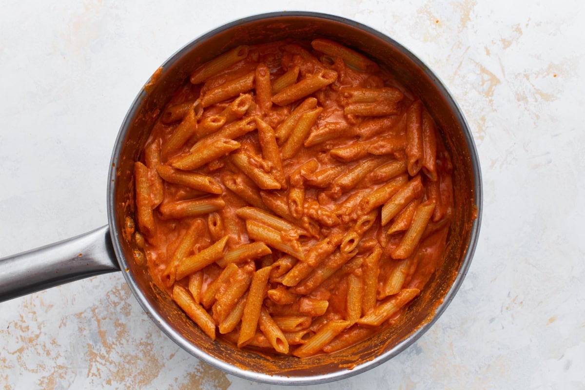Gluten-free penne tossed into the creamy vegan vodka sauce in the skillet.