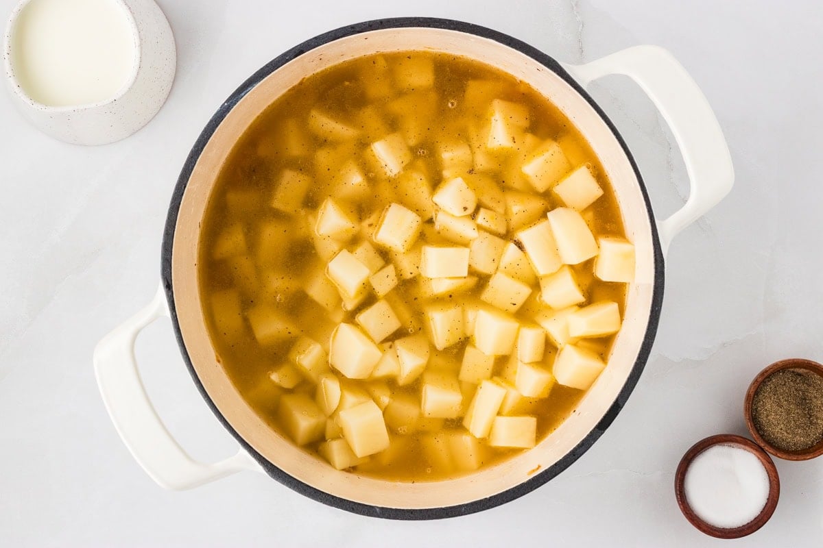 Cubed russet potatoes simmering in golden chicken broth inside a white pot, ready to cook until tender.