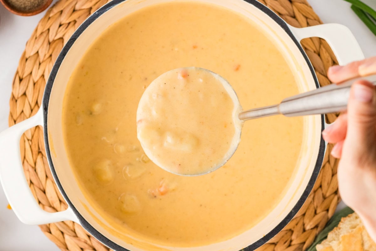 A ladle lifting a spoonful of creamy potato soup from the pot, showing the thick, hearty texture.