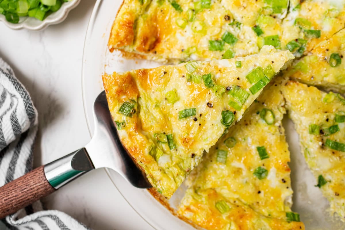 A slice of crustless zucchini quiche being lifted from the pie dish with a metal pie server.