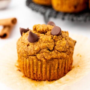 Flourless pumpkin muffin unwrapped on parchment liner, topped with melty chocolate chips and ready to eat.