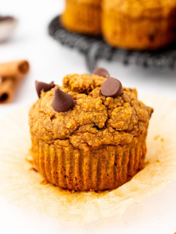 Flourless pumpkin muffin unwrapped on parchment liner, topped with melty chocolate chips and ready to eat.