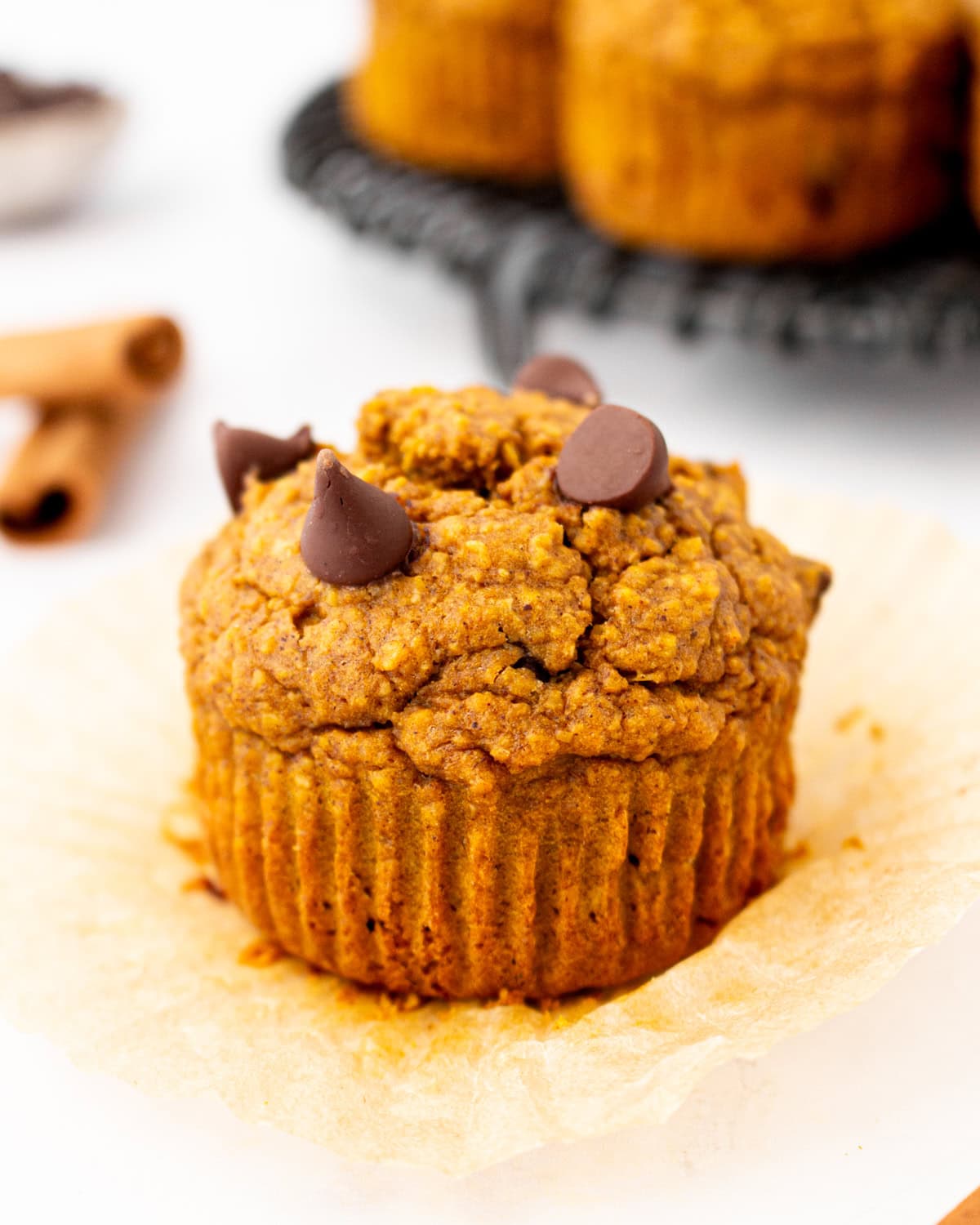 Flourless pumpkin muffin unwrapped on parchment liner, topped with melty chocolate chips and ready to eat.
